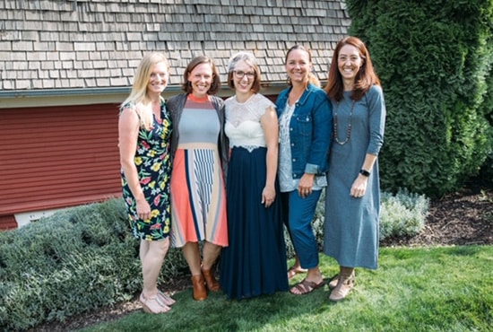 home2_s4_1 Five women, smiling under a sunny sky, stand together on a lush lawn. Clad in colorful dresses, they appear in front of a wooden building adorned with greenery. Among them is a dedicated veterinarian, embodying warmth and compassion.